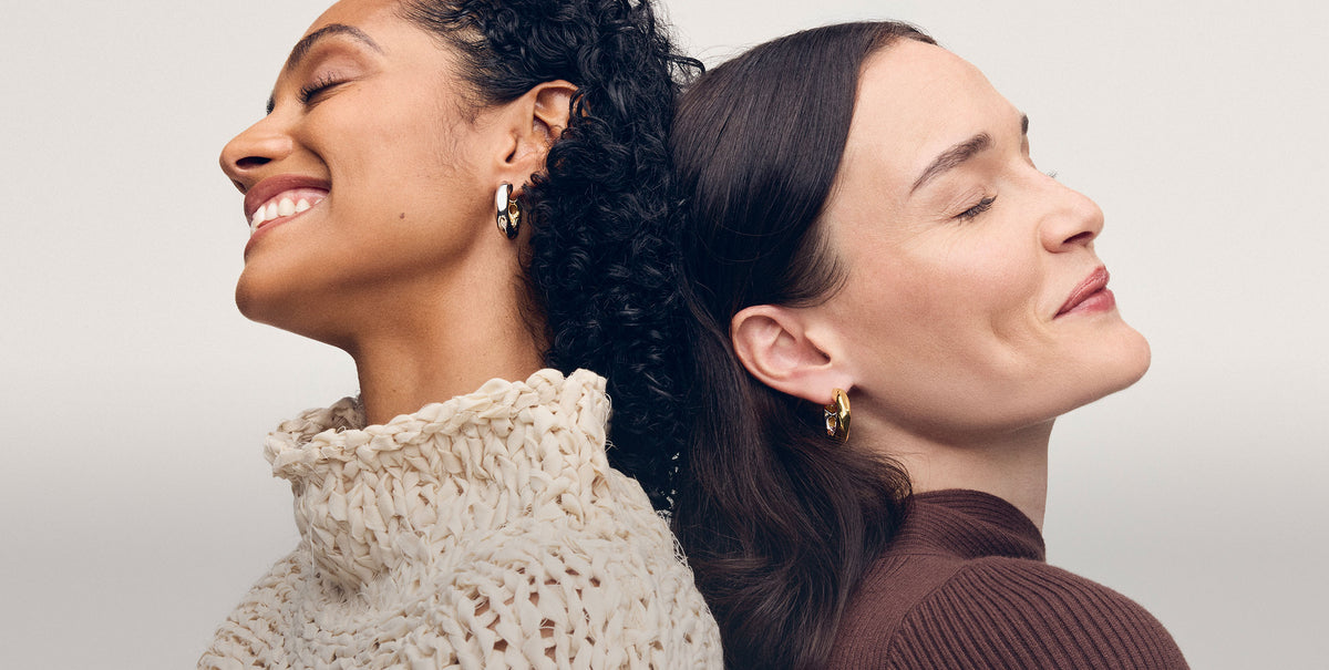 Two women wearing MACHETE wavy chunky hoop earrings in gold and 3/4 silver. 
